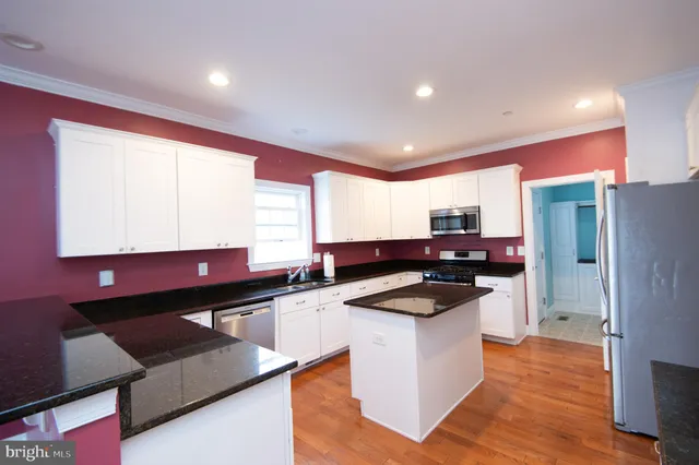 a kitchen with granite countertop a refrigerator a sink and white cabinets