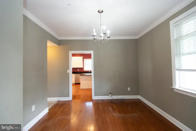 an empty room with wooden floor chandelier and windows