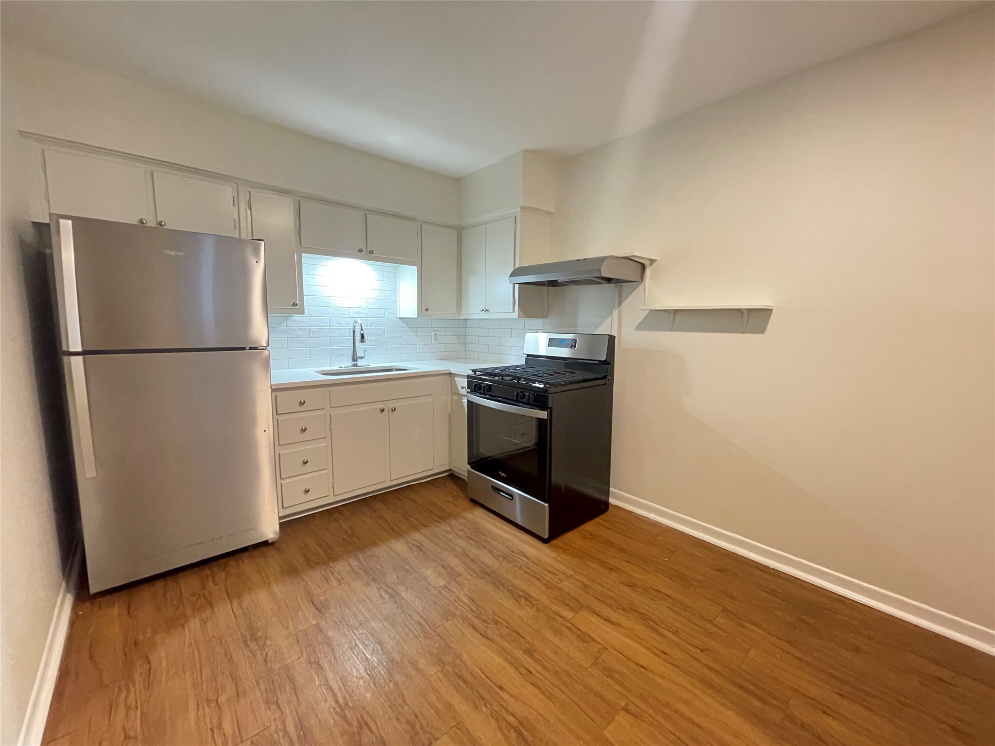 3106 Duval Street, Unit 101 Austin, TX 78705 - Photo 10 of 25 Kitchen featuring stainless steel appliances, light countertops, white cabinetry, backsplash, and light wood-style floors
