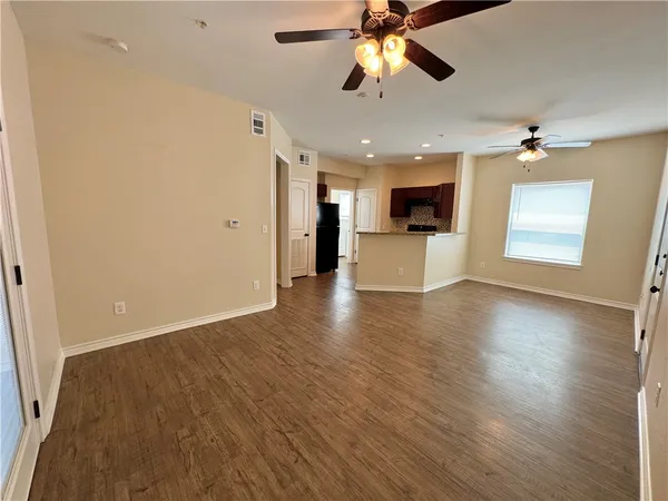 an empty room with wooden floor ceiling fan and windows