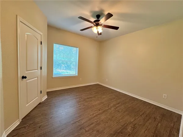 an empty room with wooden floor chandelier fan and windows