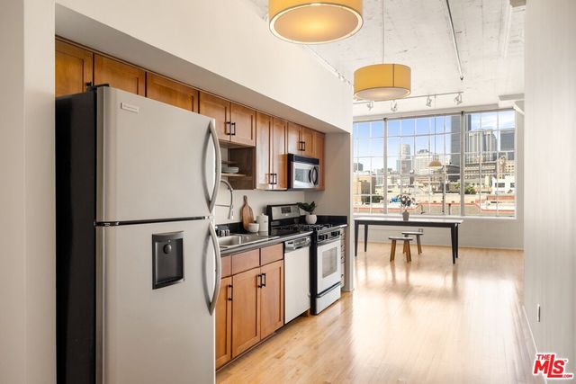 a kitchen with stainless steel appliances granite countertop a refrigerator a stove a sink a dining table and chairs with wooden floor