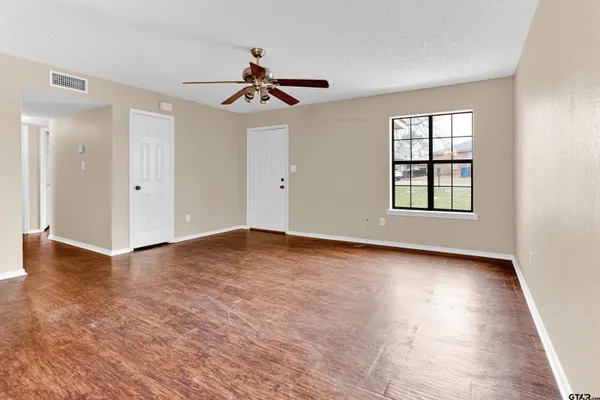 an empty room with wooden floor chandelier fan and windows