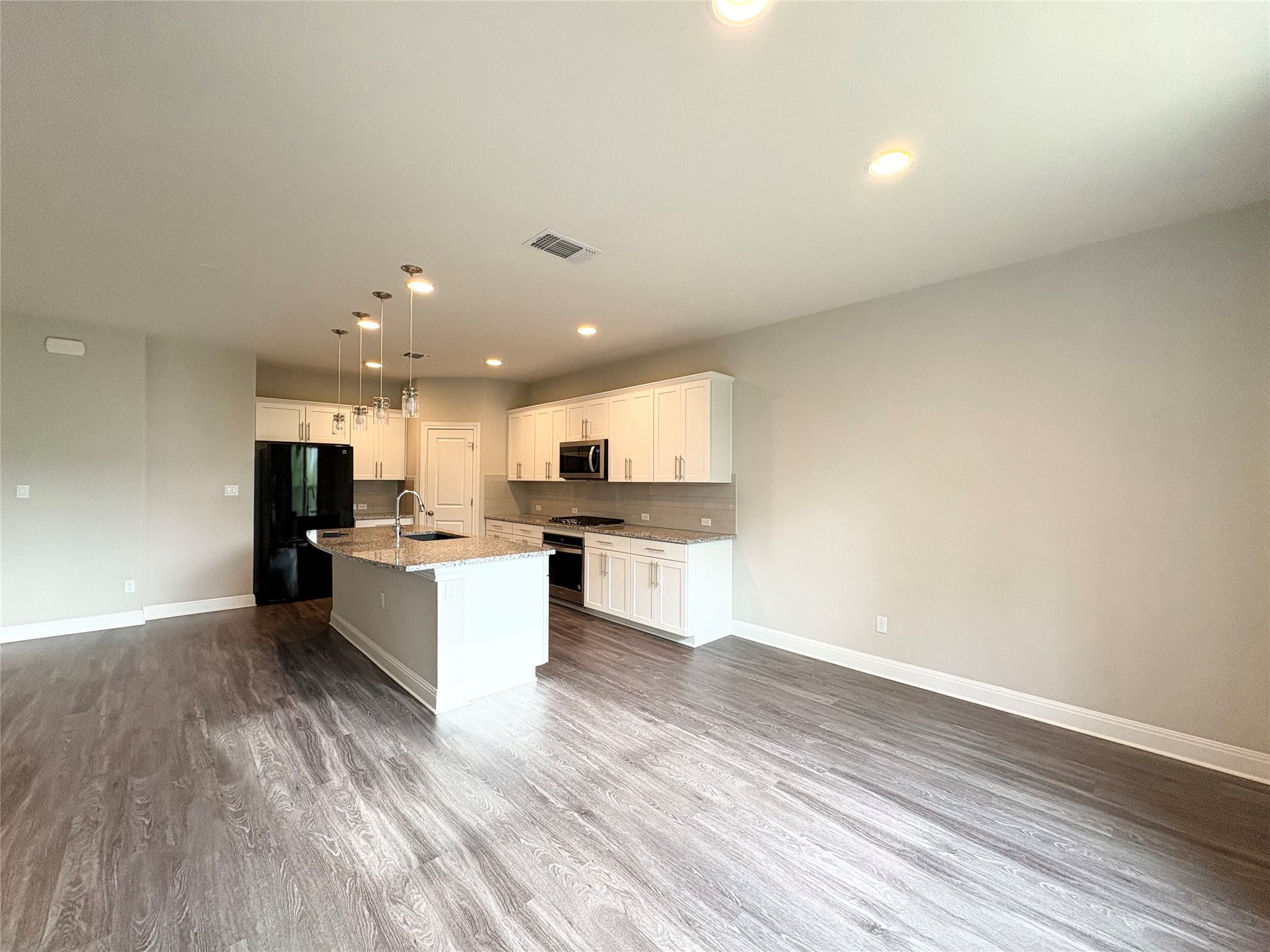 16103 Windroot Street Austin, TX 78728 - Photo 7 of 32 Plank flooring runs throughout this open kitchen featuring a central island and recessed lighting.