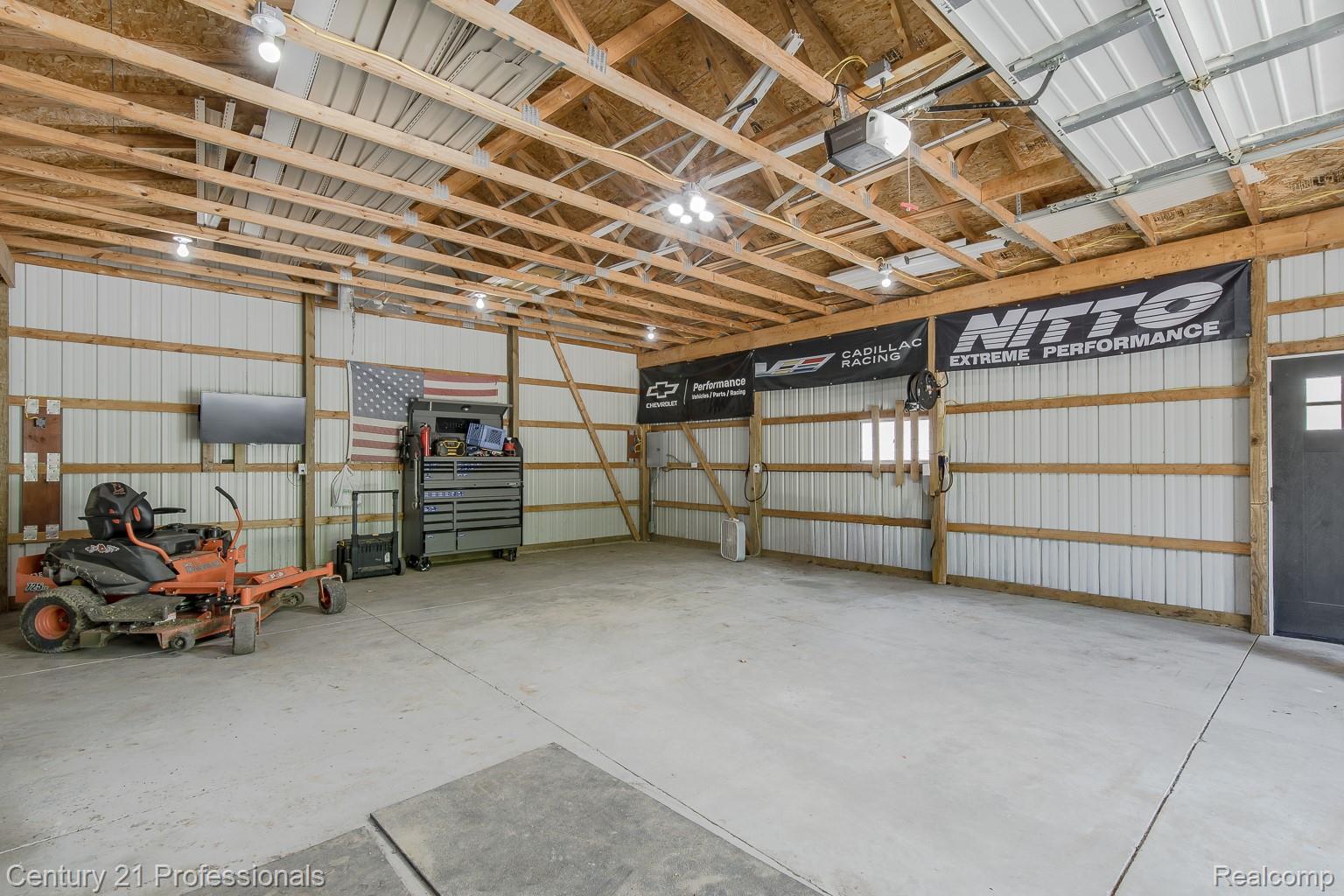 1790 Kent Road Ortonville, MI 48462 - Photo 30 of 64 Spacious utility building featuring a concrete floor, exposed wood beam ceiling, corrugated metal wall panels, multiple overhead light fixtures, and a black paneled door with window accents