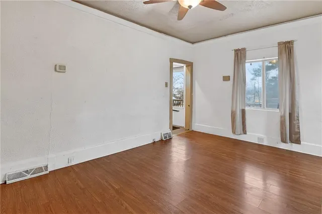 an empty room with wooden floor chandelier fan and windows