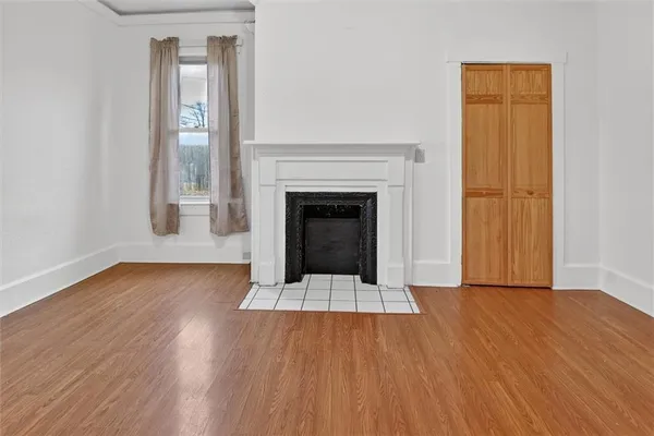a view of an empty room with wooden floor fireplace and a window