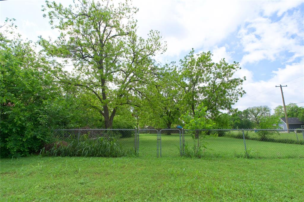 714 Potter Street Gainesville, TX 76240 - Photo 2 of 12 The property features a fenced yard with a gate, a well-maintained lawn, and mature trees providing natural shade