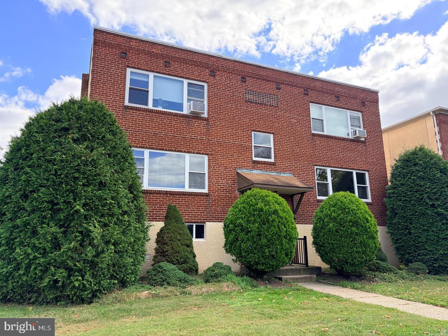 a view of a brick house with a yard plants and large tree
