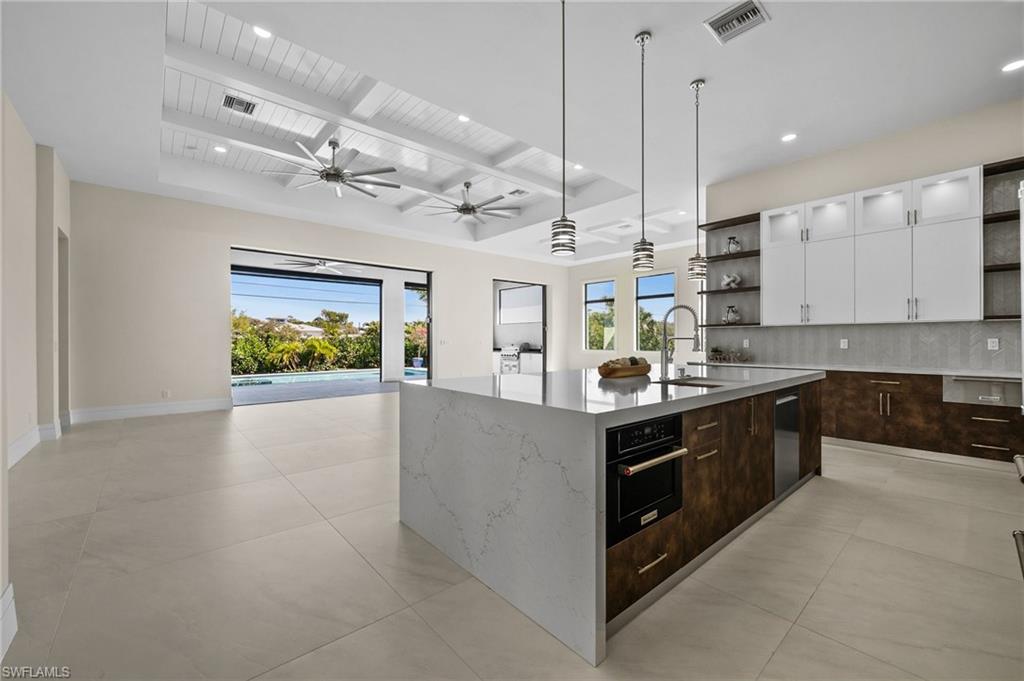 1045 Morningside Drive Naples, FL 34103 - Photo 24 of 50 Kitchen featuring open shelves, beam ceiling, dark brown cabinets, decorative backsplash, and white cabinetry