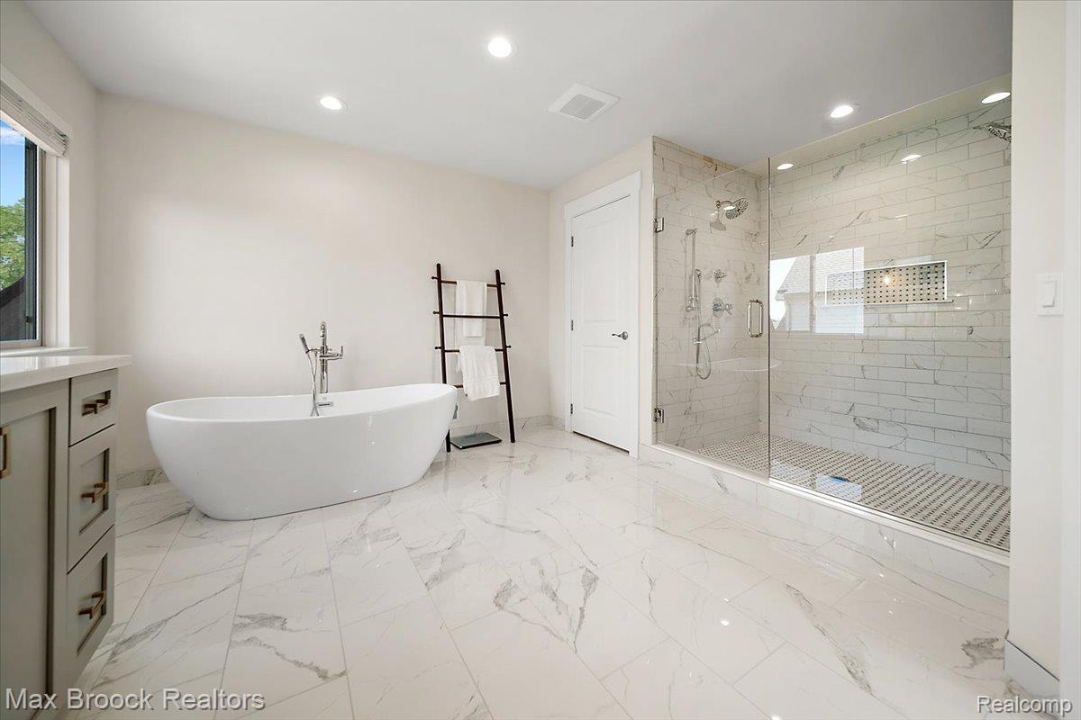 1942 Nottingham Drive Rochester, MI 48307 - Photo 52 of 97 Spacious bathroom featuring a freestanding soaking tub, a large glass-enclosed shower with subway tile, a vanity with ample storage, and marble-look tile flooring