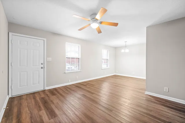 an empty room with wooden floor fan and windows