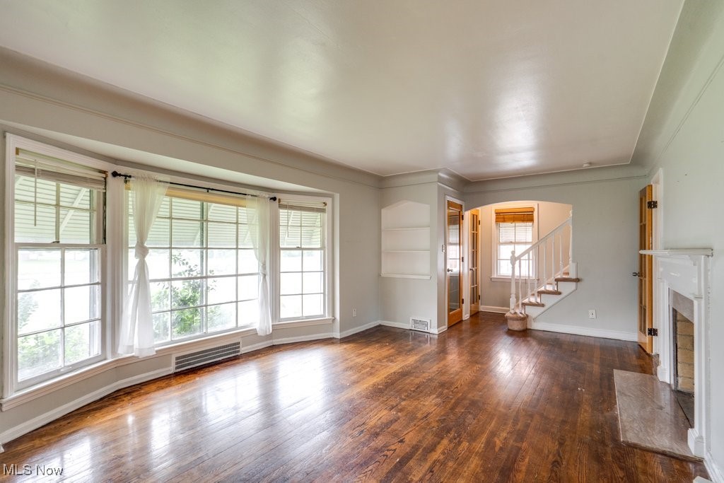 13677 Cedar Road Cleveland, OH 44118 - Photo 13 of 50 Unfurnished living room with arched walkways, dark wood-style floors, stairway, a fireplace, and ornamental molding