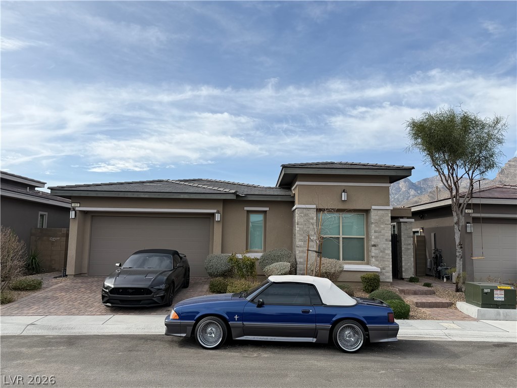Prairie-style house with an attached garage, decorative driveway, stucco siding, and a tiled roof