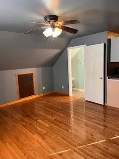 a view of an empty room with wooden floor and a kitchen
