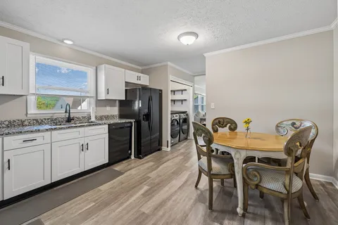 a kitchen with granite countertop stainless steel appliances a dining table chairs refrigerator and sink
