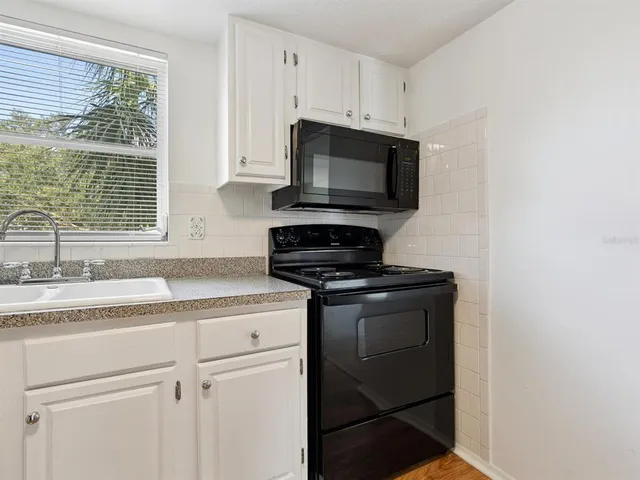 a kitchen with granite countertop white cabinets appliances and a window