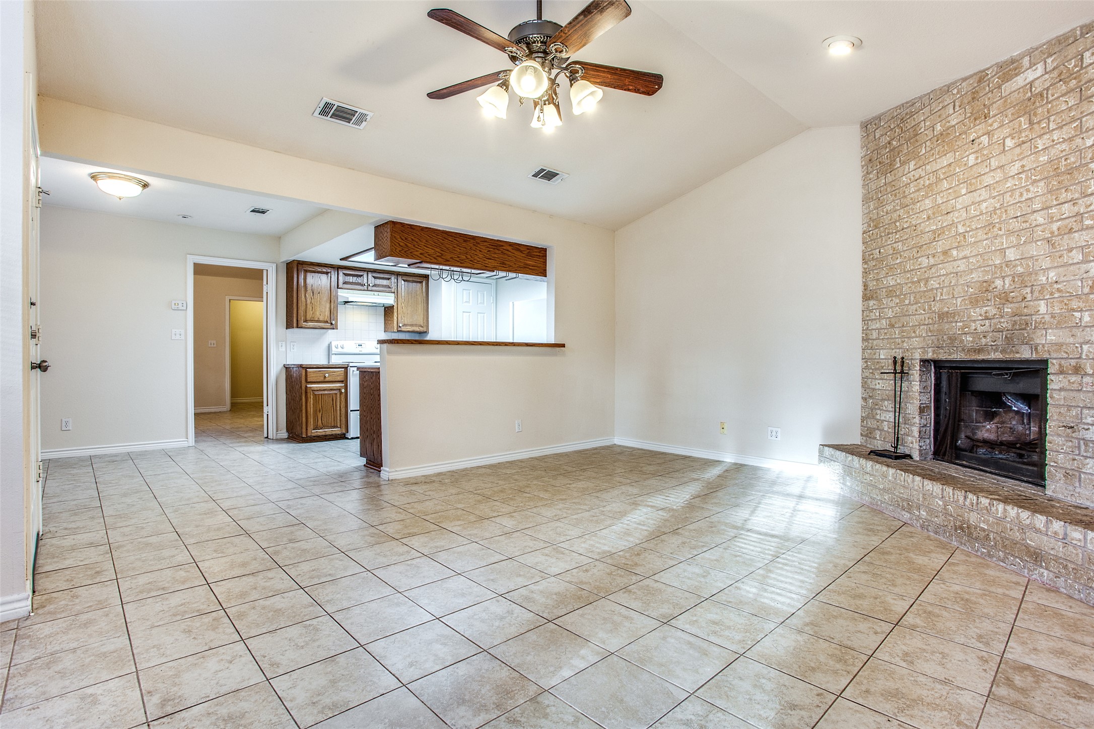 8811 Clearbrook Trail Austin, TX 78729 - Photo 18 of 38 rt B - A well-lit living area features tiled flooring and a prominent brick fireplace, adjacent to a practical kitchen pass-through.