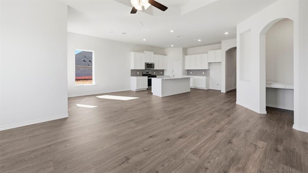 4163 Waldron Trail Forney, TX 75126 - Photo 10 of 30 Spacious open-concept interior featuring wood-finish flooring, a contemporary kitchen with a central island and white cabinetry, a built-in desk niche, recessed lighting, and a ceiling fan