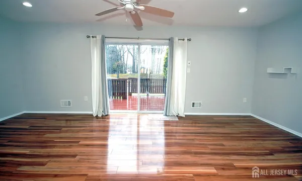an empty room with wooden floor and way to kitchen