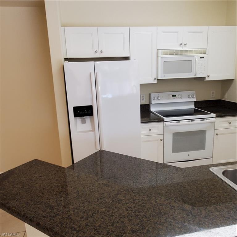 12980 Positano Circle, Unit 207 Naples, FL 34105 - Photo 6 of 23 a kitchen with granite countertop white cabinets and white appliances