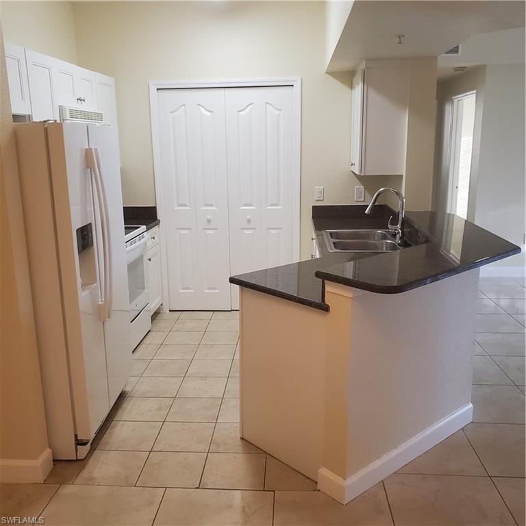 12980 Positano Circle, Unit 207 Naples, FL 34105 - Photo 8 of 23 a kitchen with stainless steel appliances a refrigerator a sink and white cabinets