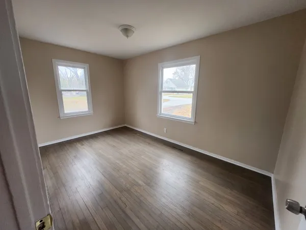 a view of an empty room with wooden floor and window