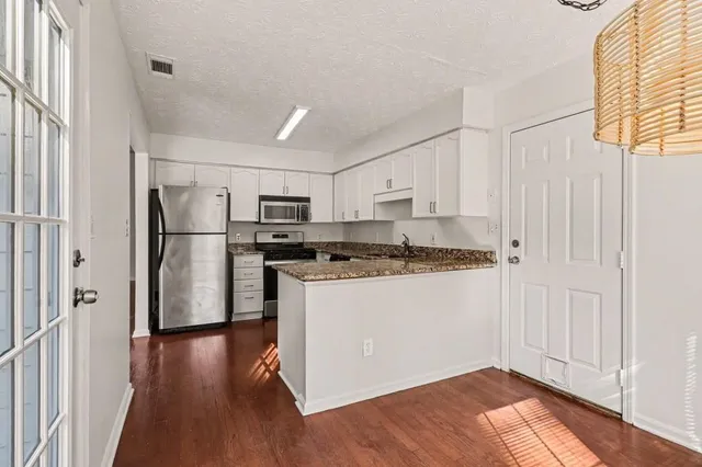 a kitchen with stainless steel appliances granite countertop a refrigerator a sink and white cabinets with wooden floor