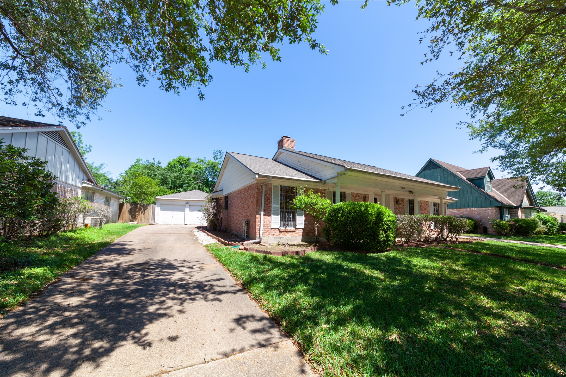 8826 Roos Road Houston, TX 77036 - Photo 38 of 42 Charming single-story home with a welcoming front porch, set on a spacious lot with mature trees. The driveway leads to a detached garage, offering ample parking. The yard is well-maintained, providing a peaceful and inviting atmosphere.