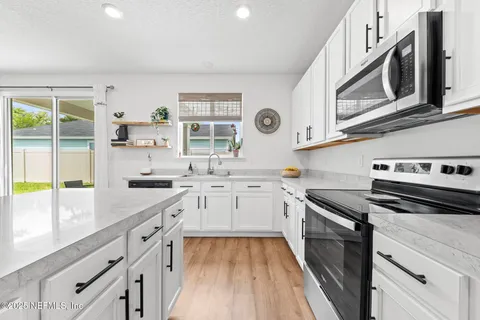 a kitchen with stainless steel appliances a stove a sink a dining table and chairs with wooden floor