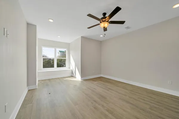 an empty room with wooden floor fan and windows