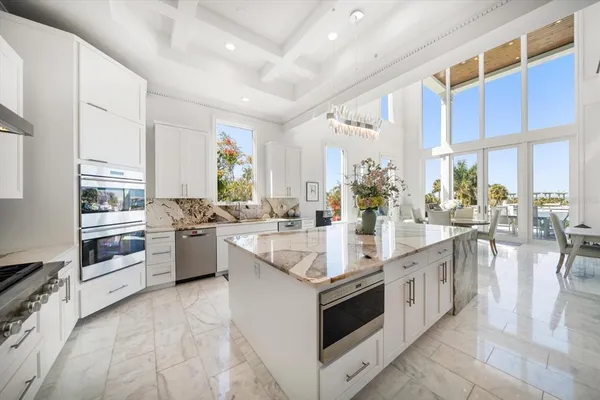 a large white kitchen with stainless steel appliances granite countertop a lot of counter space and a view of living room