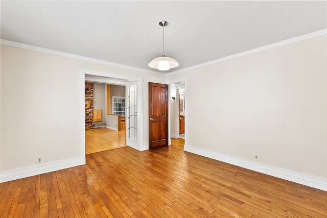 a view of an empty room with window and hardwood floor
