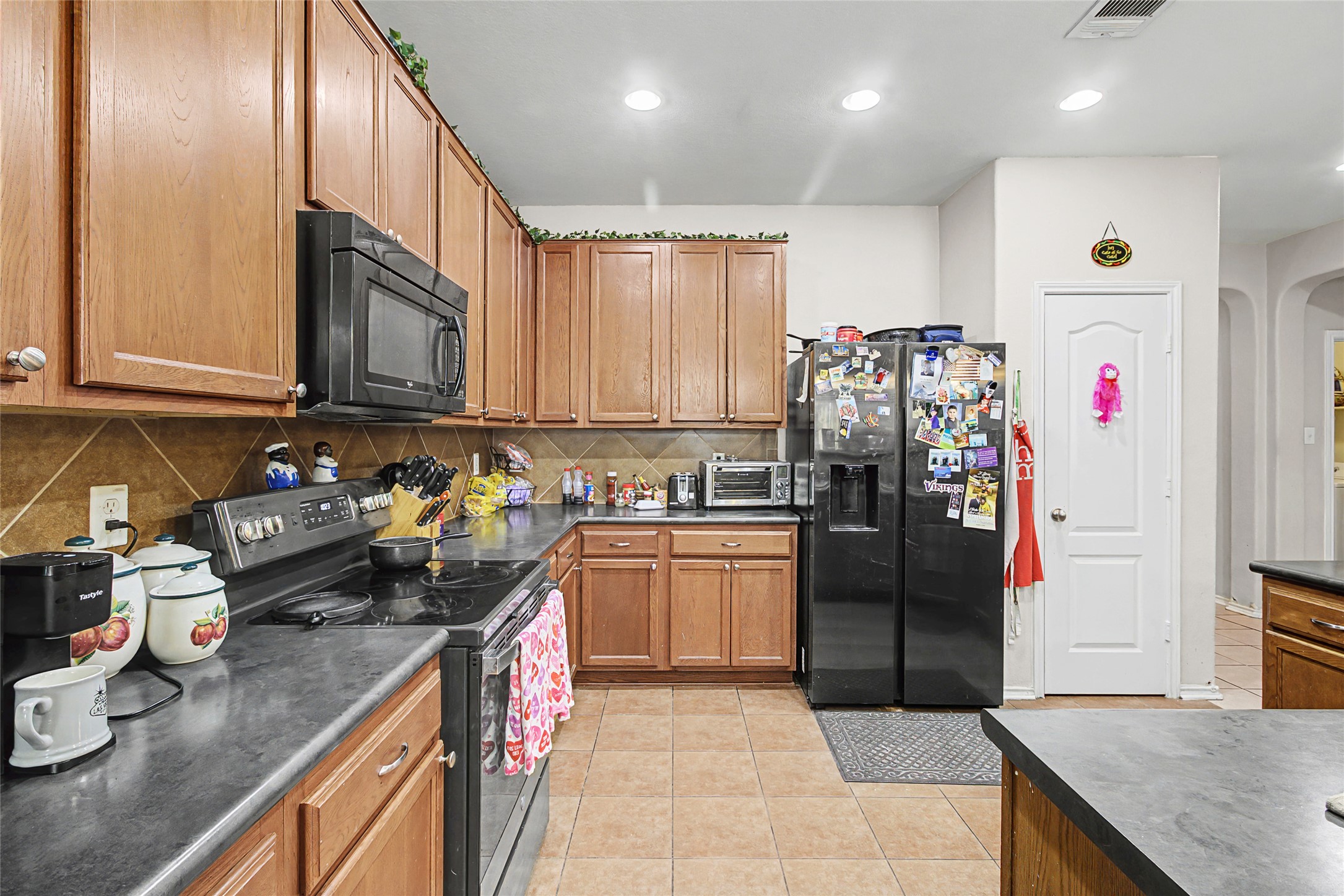 344 Matthews Kyle, TX 78640 - Photo 5 of 15 Kitchen with dark countertops, black appliances, wood finish cabinetry, arched walkways, and light tile patterned floors