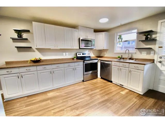 a kitchen with stainless steel appliances granite countertop a refrigerator a sink dishwasher a stove and white countertops with wooden floor