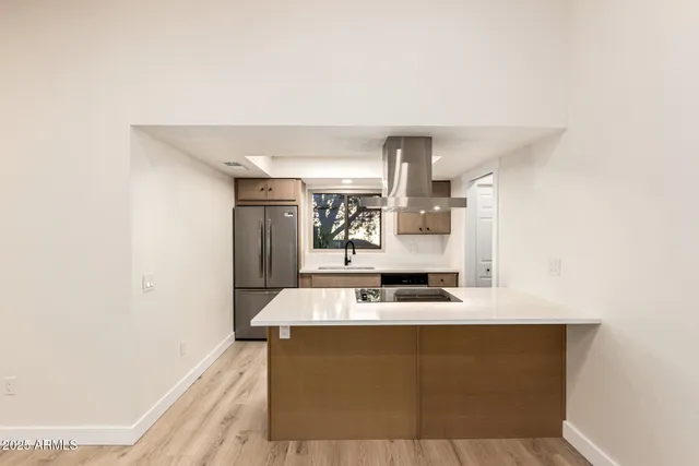 a room with kitchen island a sink a stove and a refrigerator with wooden floor