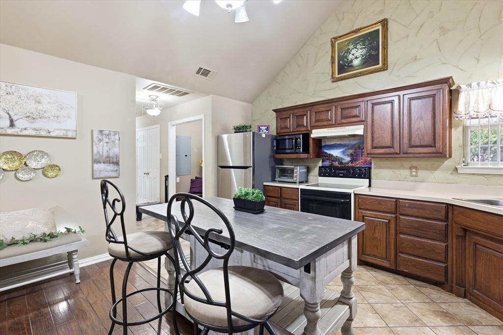 5855 Ge Horton Road Justin, TX 76247 - Photo 8 of 34 Kitchen with vaulted ceiling, wood-finish cabinetry, tile flooring, and a stainless steel refrigerator