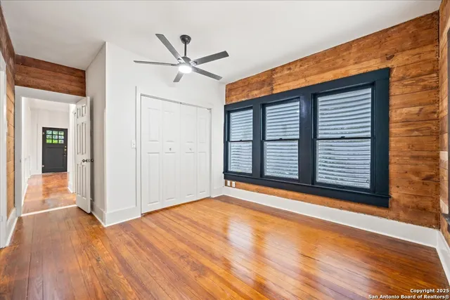 an empty room with wooden floor ceiling fan and window