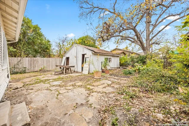 a view of a white house with a large tree and wooden fence