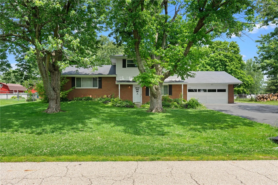 Mature trees shade the front yard of this classic brick and siding residence, featuring an attached garage and a neatly kept lawn.