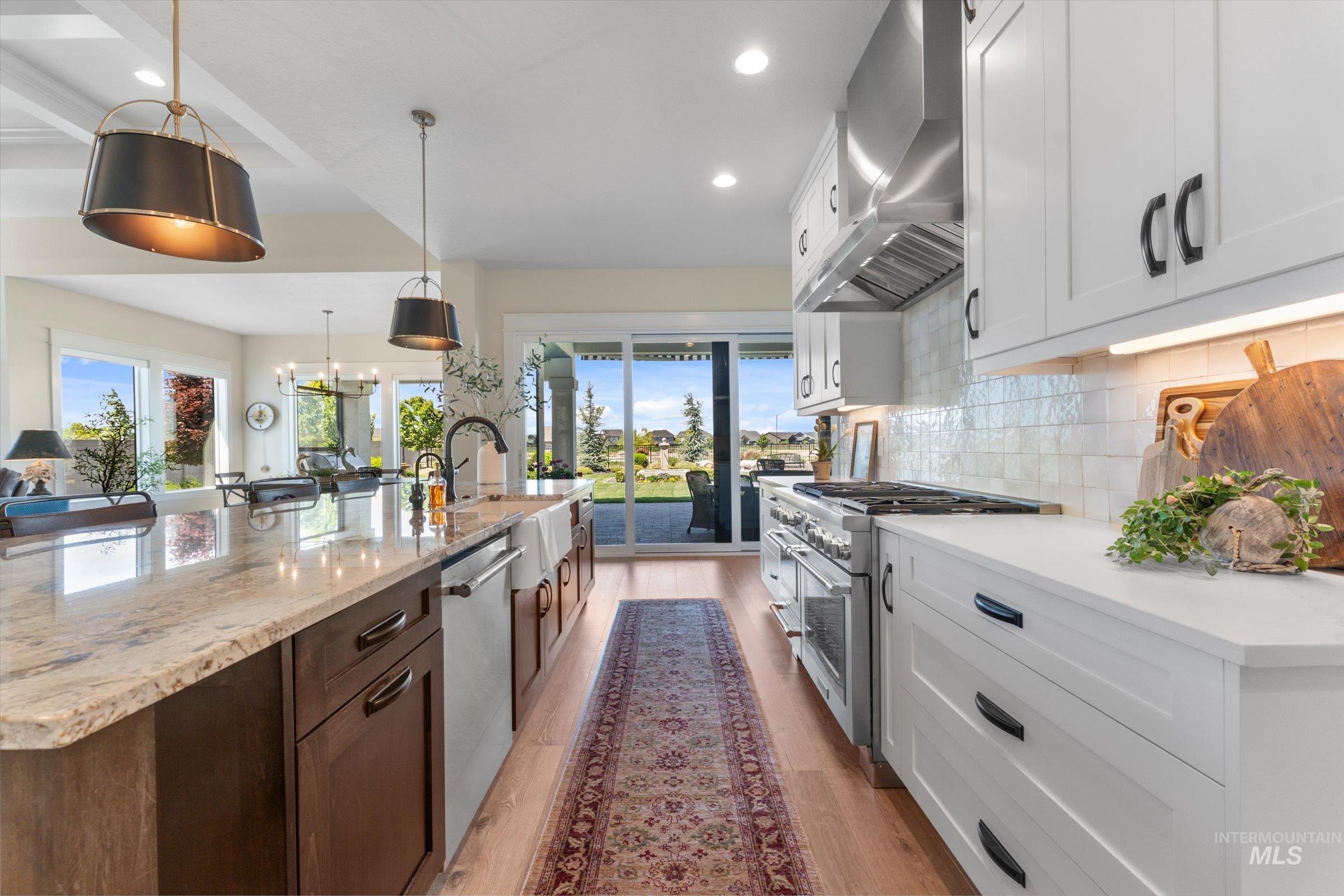 6585 South Pemberley Way Meridian, ID 83642 - Photo 13 of 43 Gourmet kitchen featuring a large island with a stone countertop, a farmhouse sink, stainless steel appliances, white shaker cabinetry, and wood-finish flooring