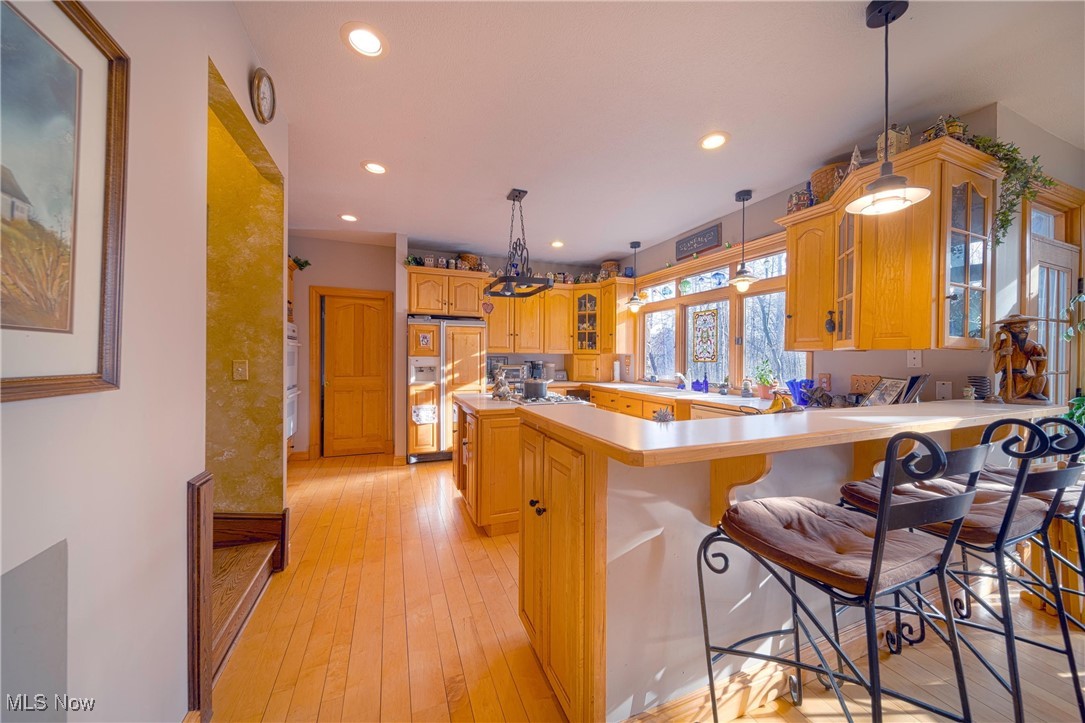 Kitchen with light hardwood / wood-style floors, paneled refrigerator, a breakfast bar, pendant lighting, and kitchen peninsula