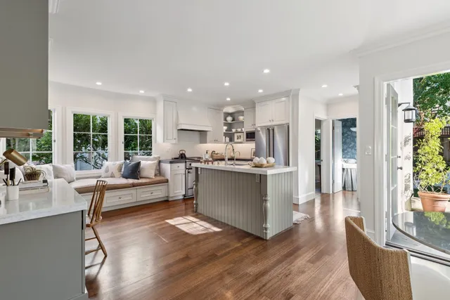 a kitchen with stainless steel appliances granite countertop a refrigerator a stove a sink a dining table and chairs with wooden floor