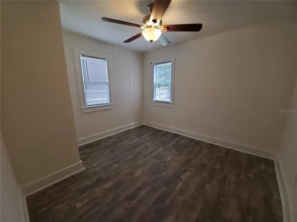an empty room with wooden floor fan and windows