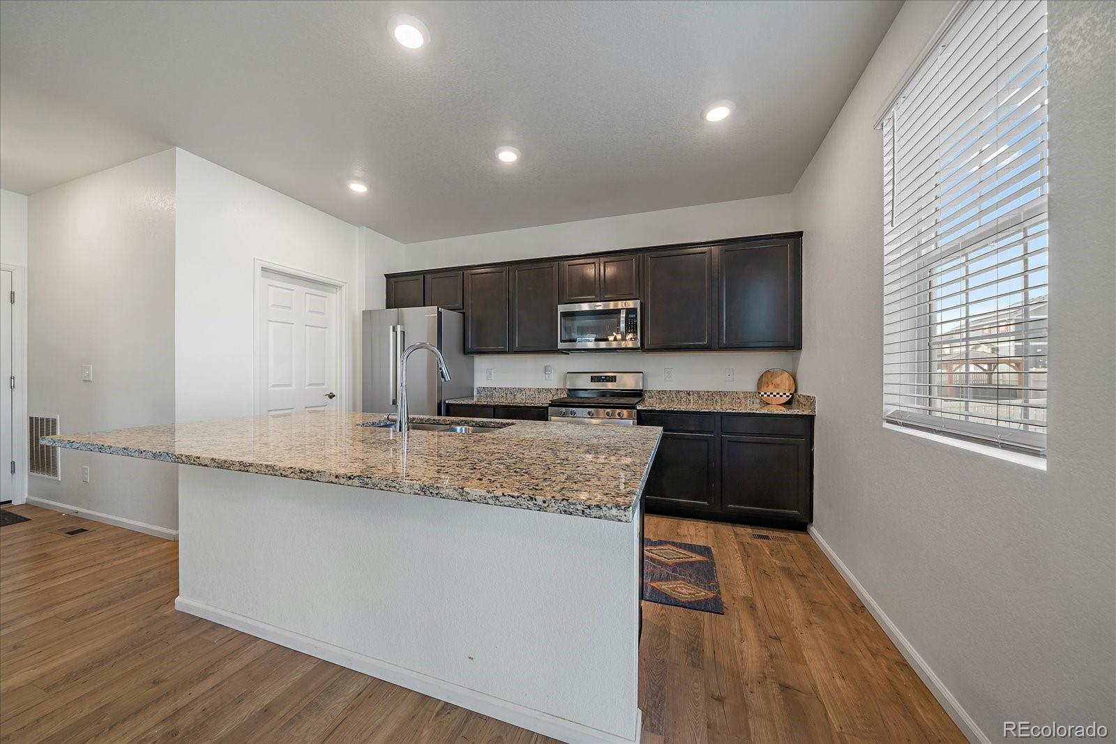 10097 Cedar Street Firestone, CO 80504 - Photo 10 of 37 a large kitchen with granite countertop a sink a stove a microwave a counter top space and cabinets