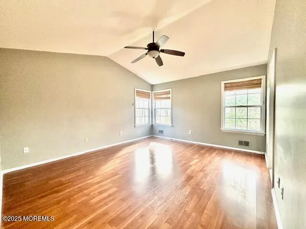 an empty room with wooden floor ceiling fan and windows