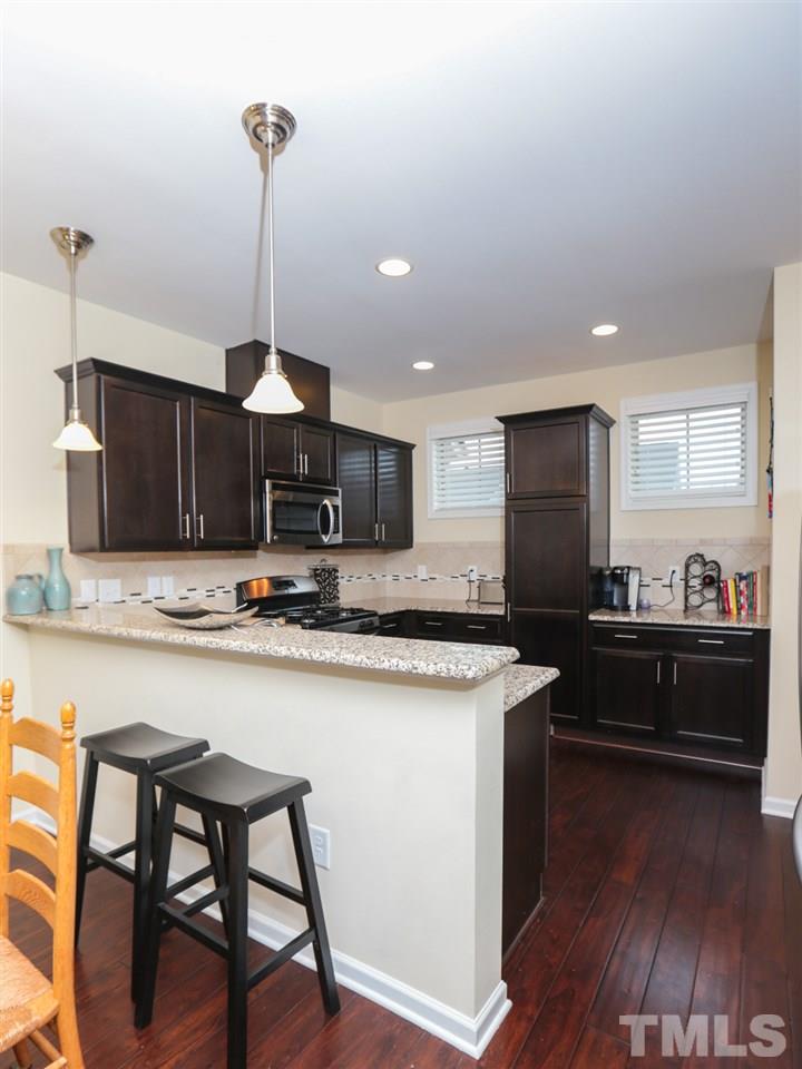 1543 Crafton Way Raleigh, NC 27607 - Photo 8 of 25 a kitchen with stainless steel appliances kitchen island granite countertop a stove top oven a sink a dining table and chairs with wooden floor