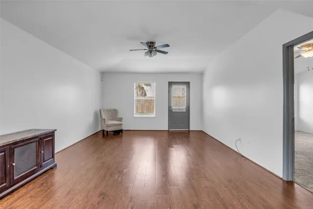 an empty room with wooden floor chandelier fan and windows