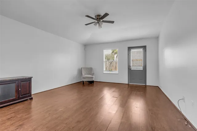 an empty room with wooden floor chandelier fan and windows