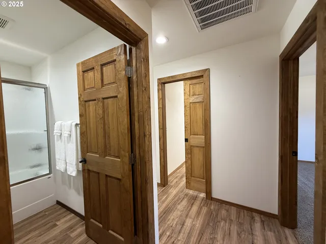 a view of a hallway with wooden floor and a bathroom
